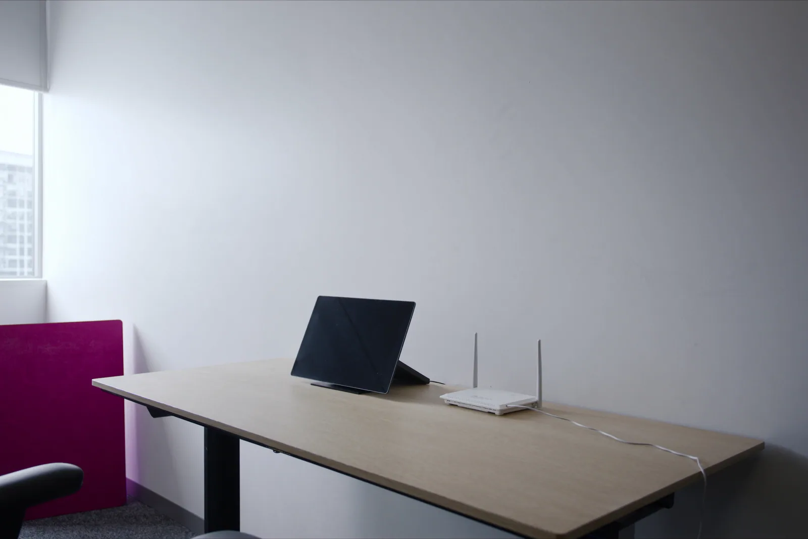 A desk phone with a dark screen and a small white router on an office desk