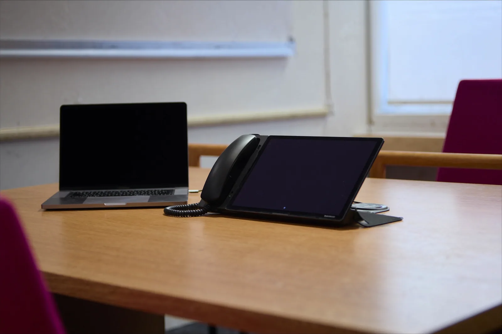 A laptop and a modern desk phone with a large dark screen on a meeting-room table